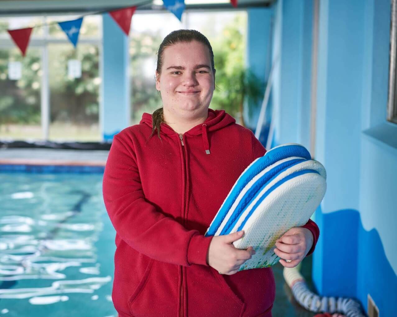 Maddy smiles holding floats next to a pool