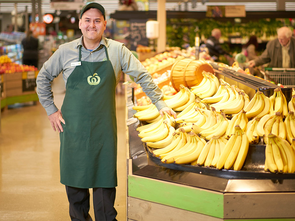 Caley smiling next to bananas at the supermarket APM helped him secure a job