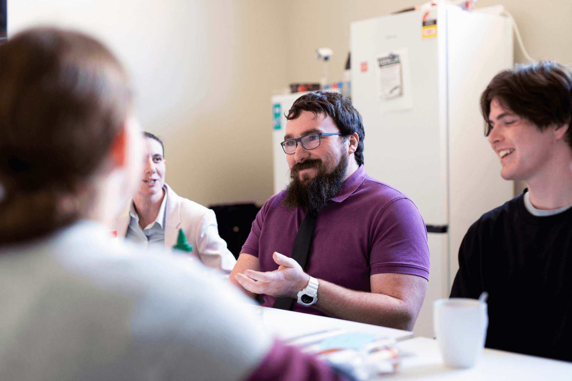 Louis smiles in a team meeting with colleagues sat round a table 