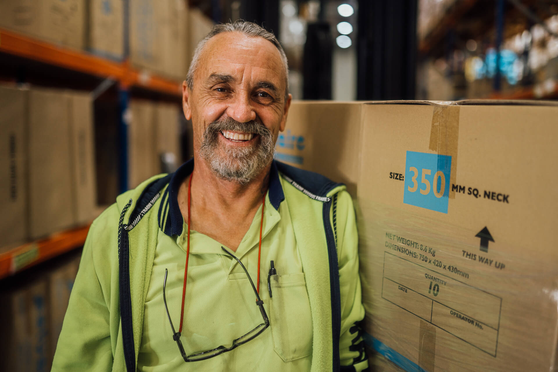 Mark in a high vis top smiles next to boxes in a warehouse