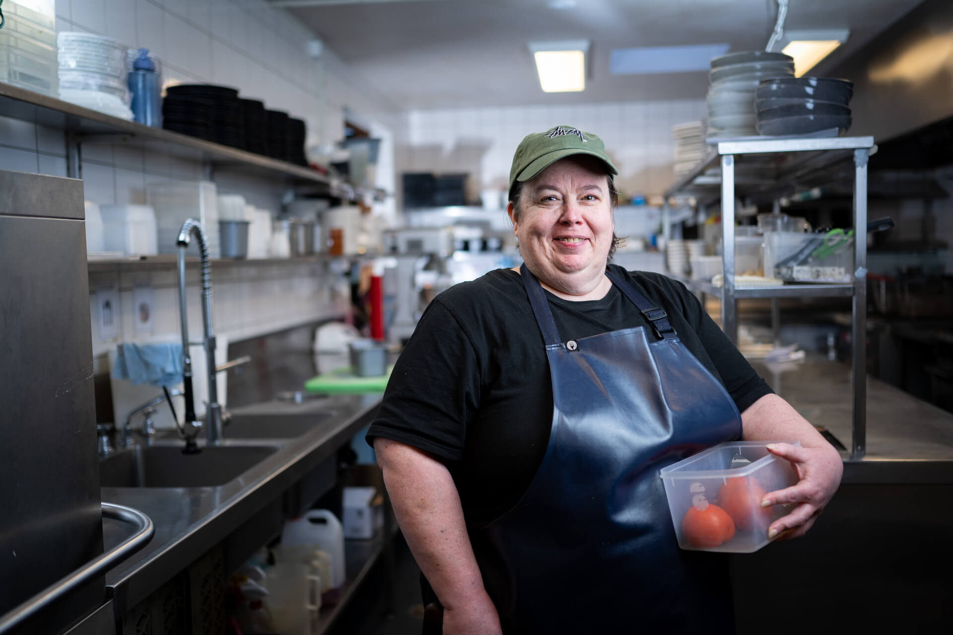 Melissa holds a tub of food in the kitchen where she works