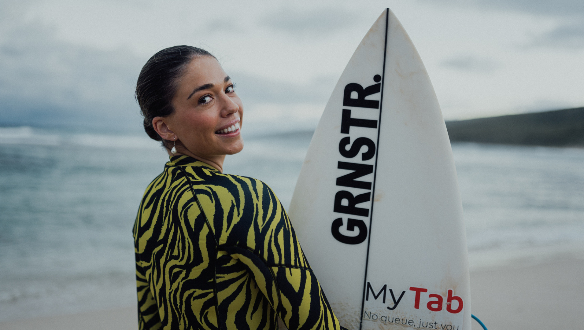 A woman smiles with a surf board at the beach