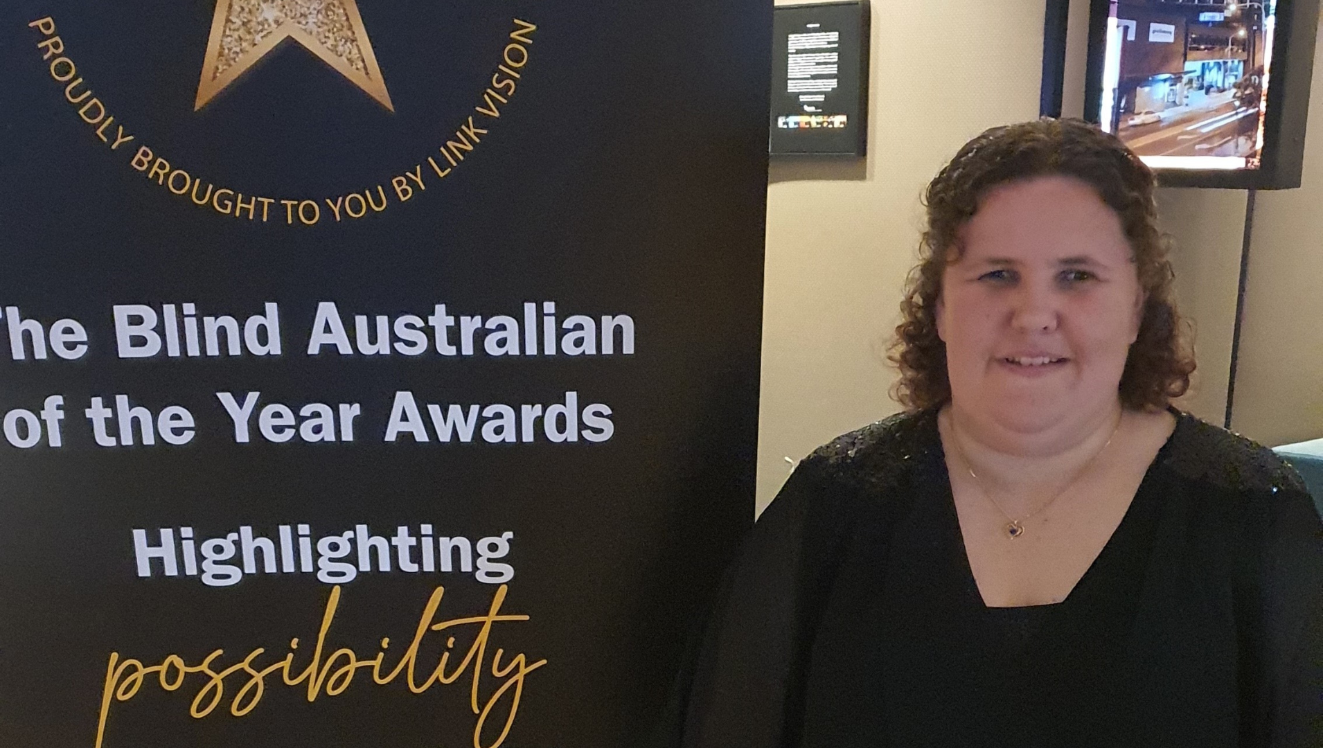 Ayesha in front of an event banner at the awards ceremony