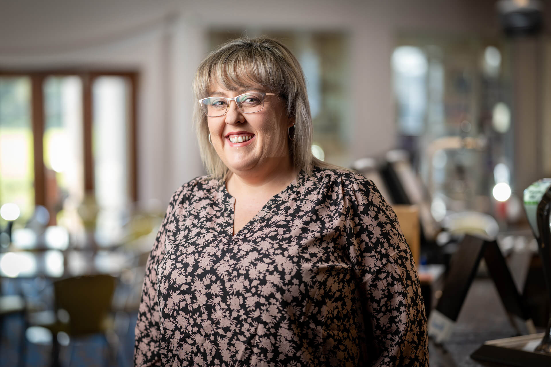 A woman with a floral top smiles in a community centre