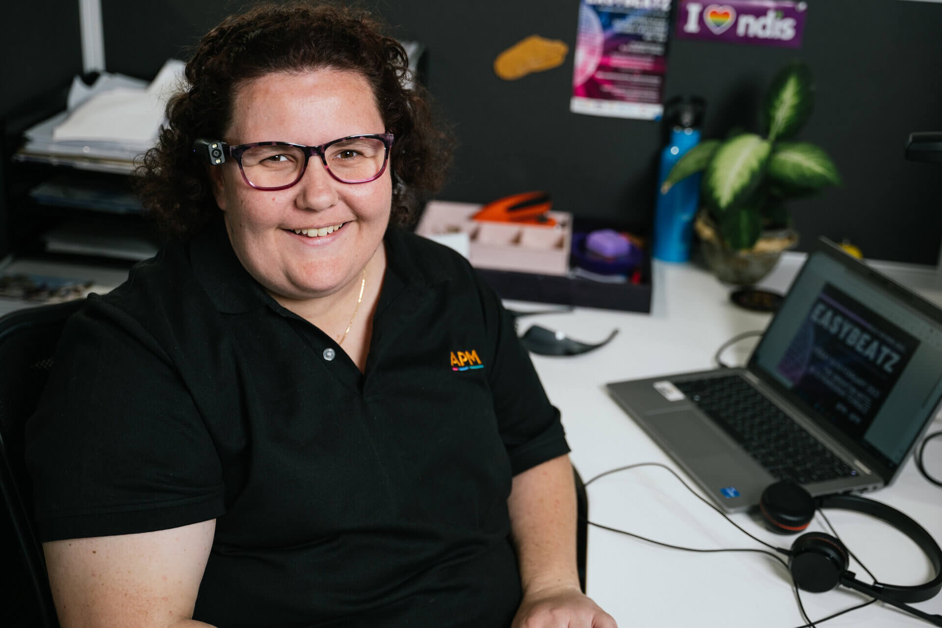 Aleysha in a black APM top sitting at a desk