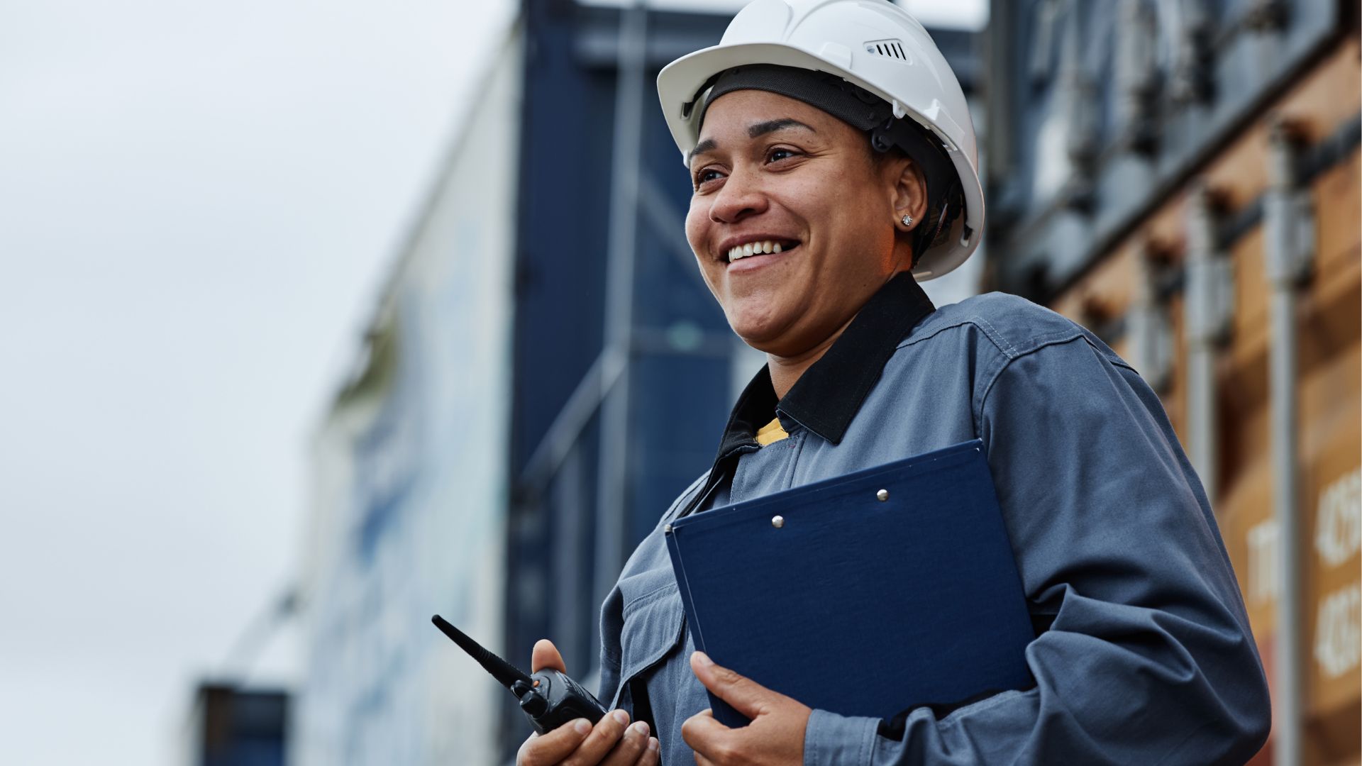 Indigenous woman in hard hat holds clipboard and walkie talkie