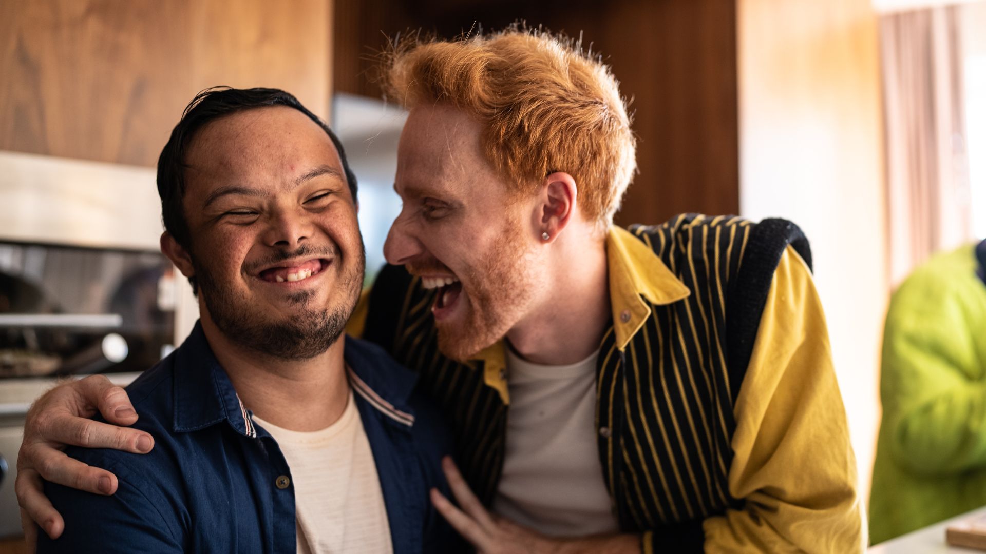 A man with Down syndrome smiles with a friend in a kitchen