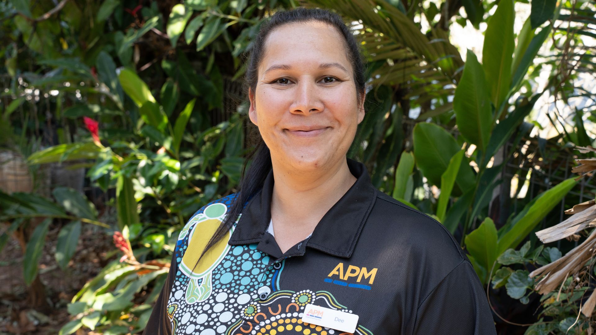 Dee stands in an APM First Nations top in front of a garden