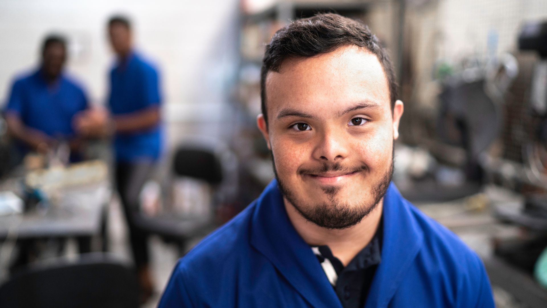 A young man with a disability in a blue overall and workplace