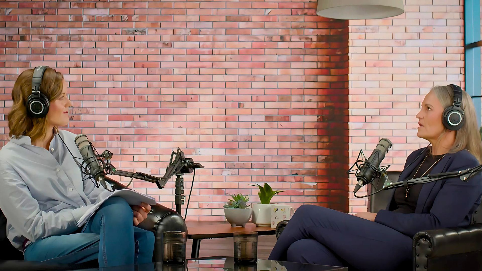 Two people sitting opposite eachother with headphones and podcast recording gear