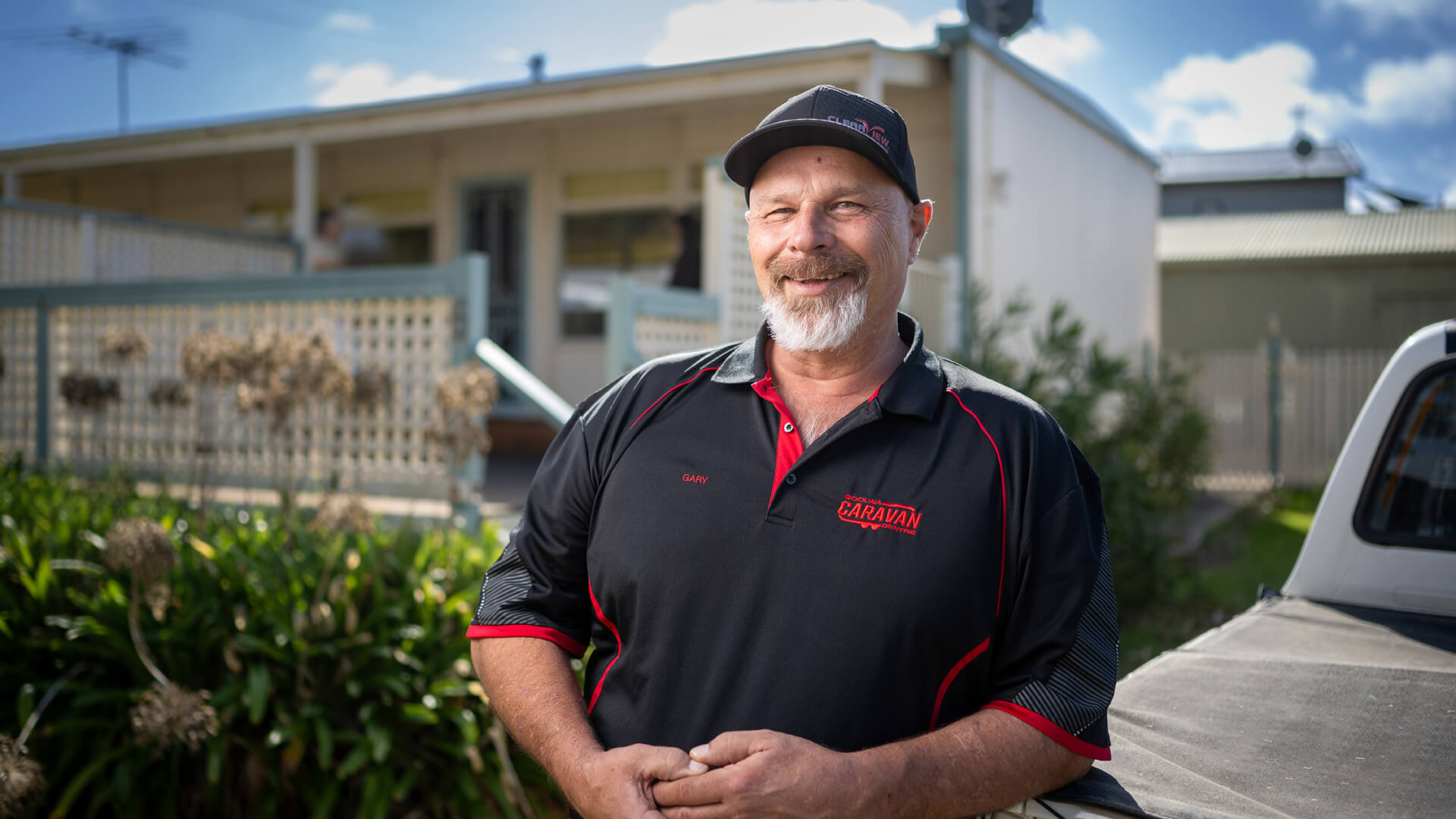 Man in black cap and shirt smiling outside his home