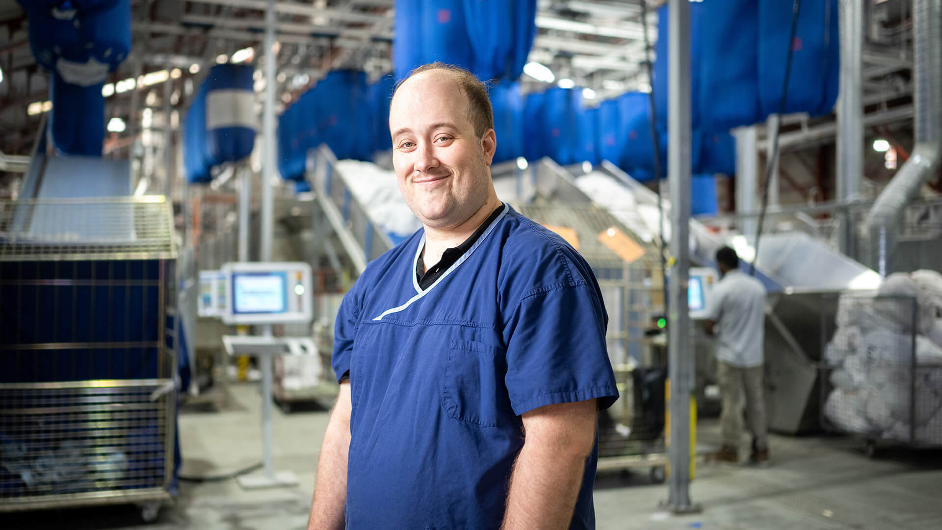 Stephen smiles in a blue tshirt in a warehouse