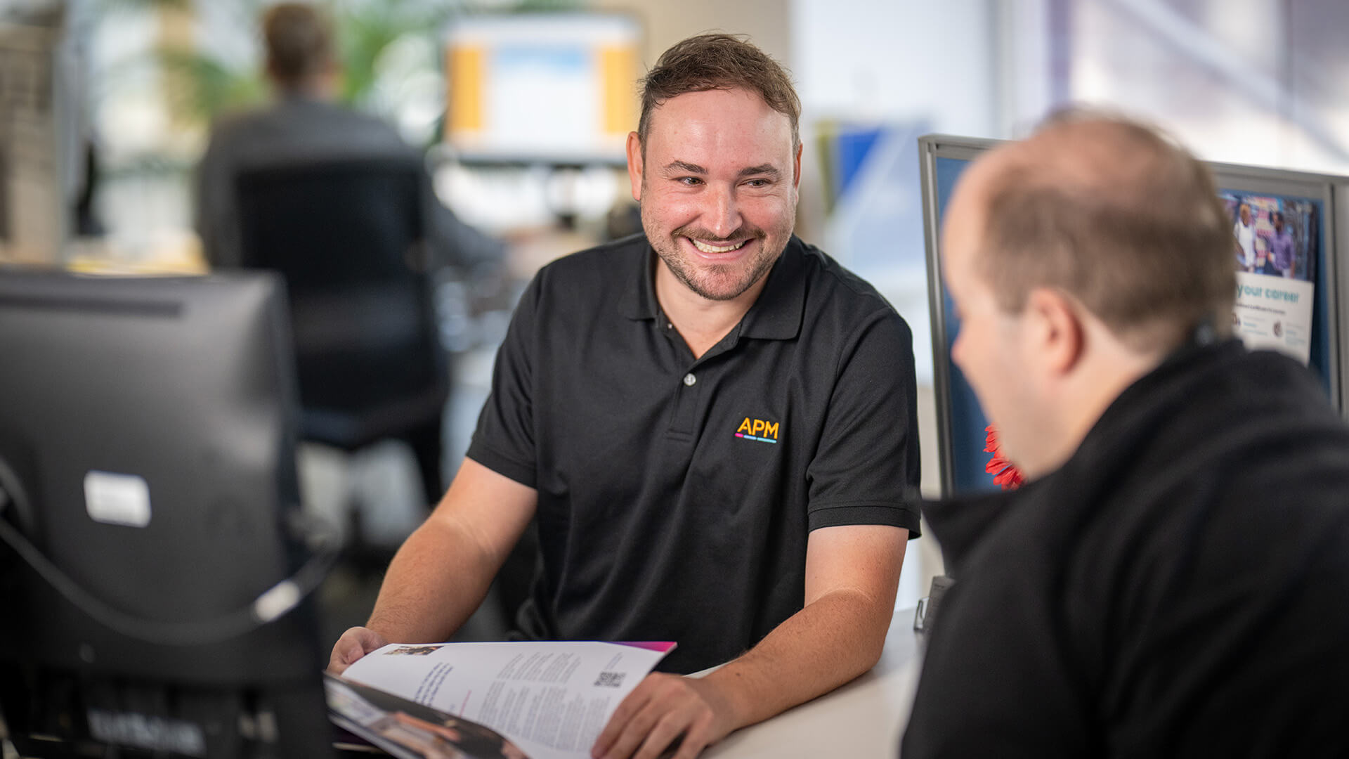 APM employment consultant in an office smiling and listening to job seeker