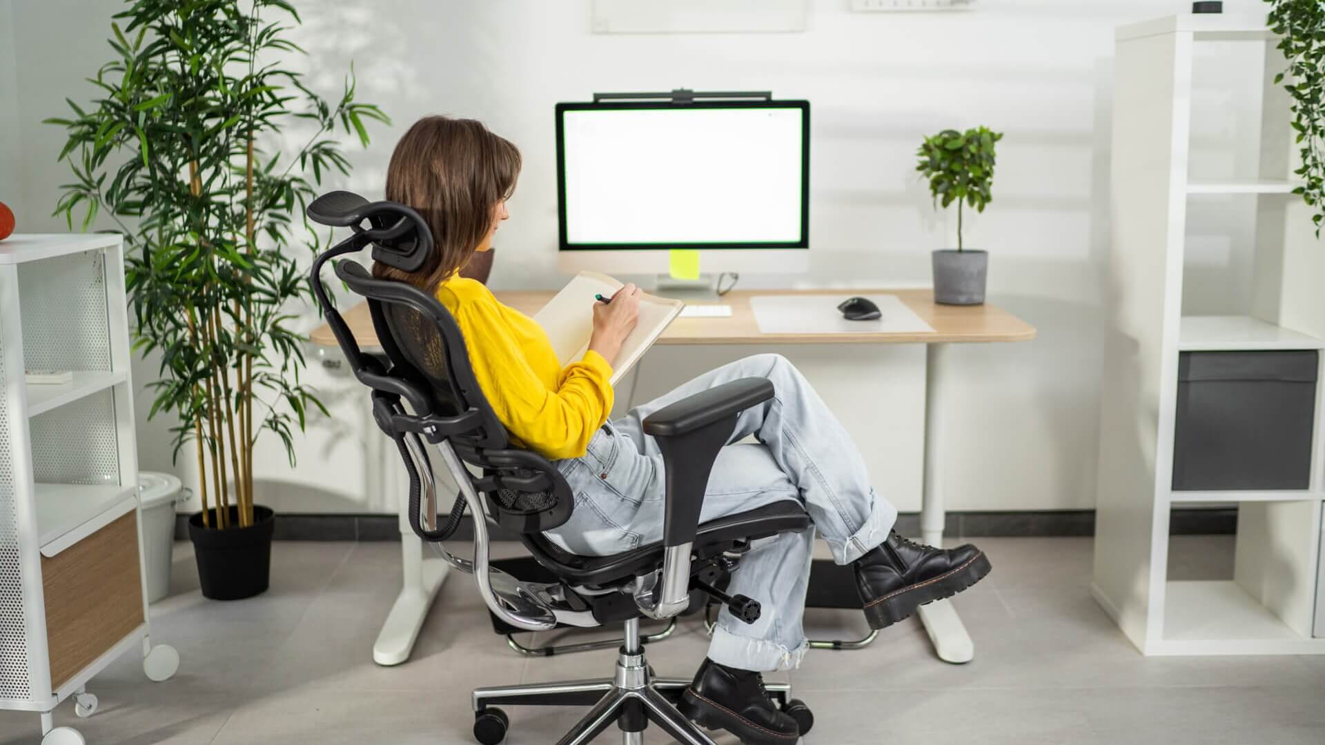 A woman sitting at a desk in her home office and writing in a notebook