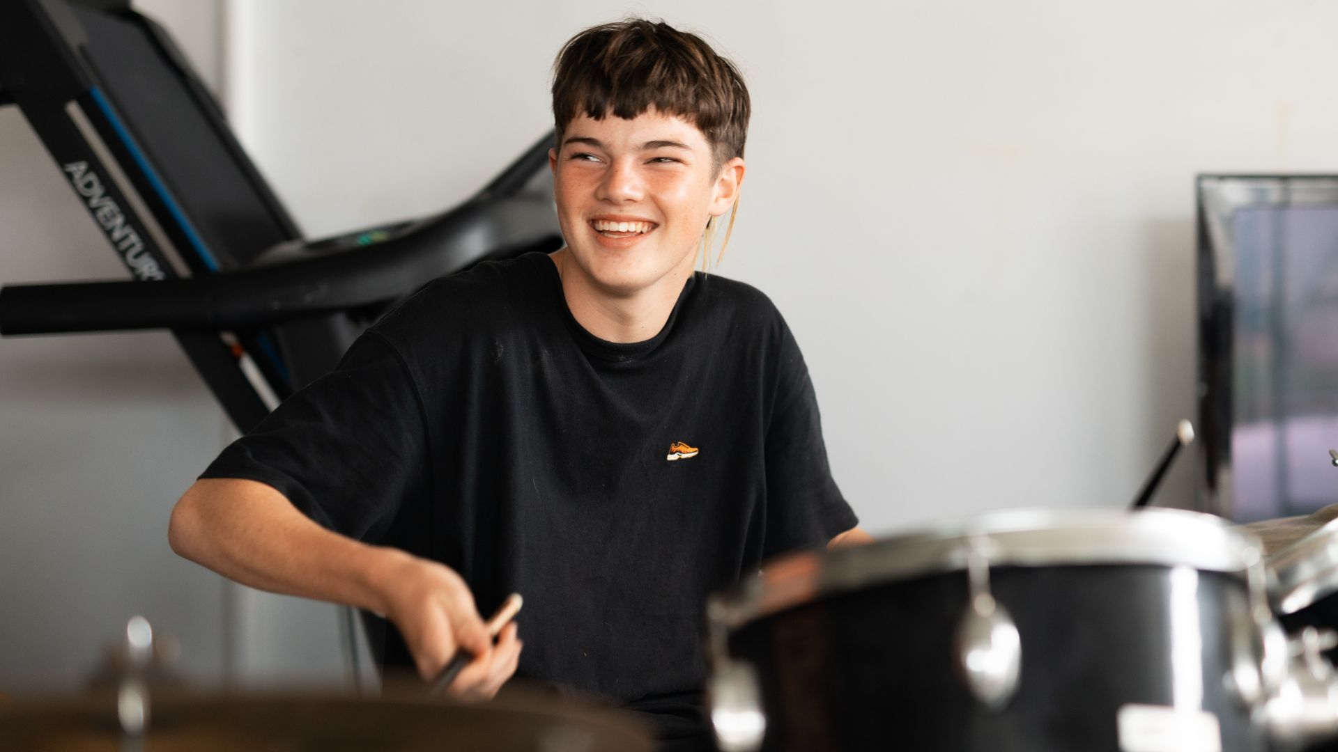 A young boy smiling while playing a set of drums