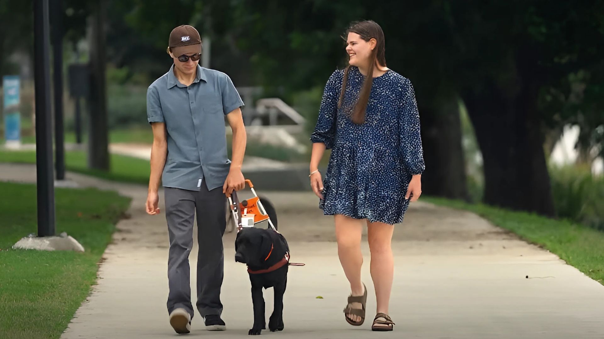 Ben and guide dog Grainger walking in a park with Ben's partner